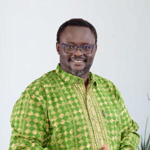 Arthur Larok stands in a green shirt, and smiles at the camera